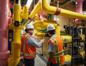 Two workers inside the water treatment plant. Yellow and pink pipes.