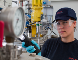 Woman checking plant's machinery - wearing safety hat and glasses.